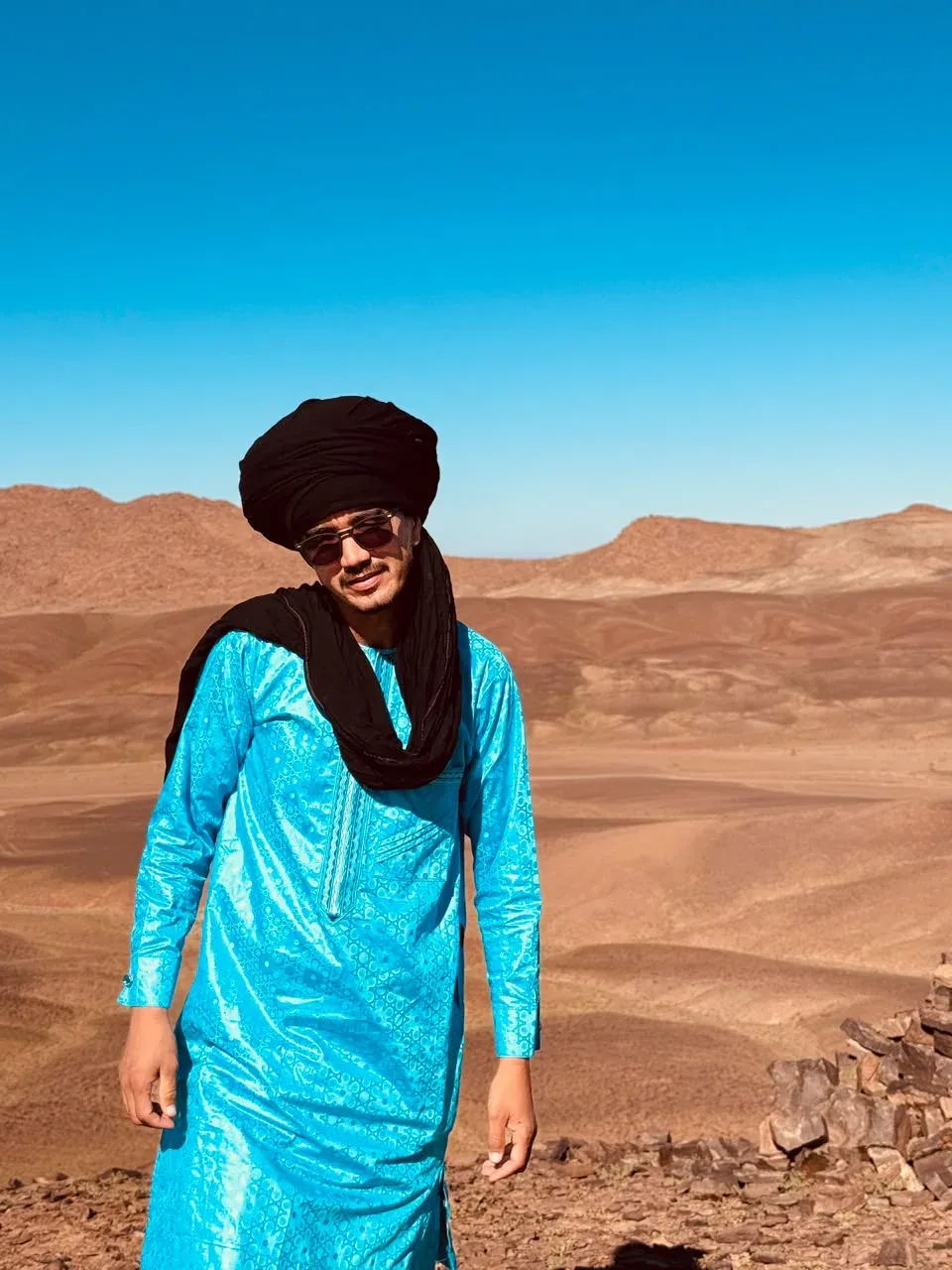 Mohamed dressed in blue, with a desert landscape behind him